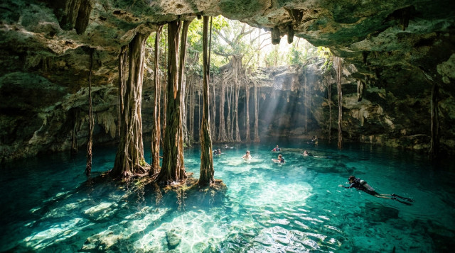 Un cenote semiabierto en la Riviera Maya con aguas turquesas cristalinas, raíces de árboles colgando desde el techo de roca y rayos de sol iluminando el fondo calizo