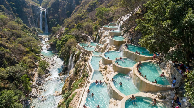 Vista aérea de las famosas pozas de aguas termales de las Grutas de Tolantongo escalonadas en la ladera de la montaña con turistas disfrutando del paisaje