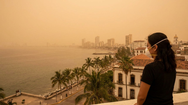 Infografía detallada que muestra a una persona usando cubrebocas frente a un horizonte brumoso por el polvo del Sahara en una ciudad costera de México