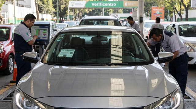 Un automóvil moderno pasando la prueba de emisiones en un verificentro con el técnico revisando los niveles en una pantalla digital y el engomado de verificación vehicular visible