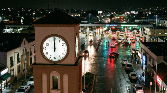 reloj marcando la 1:00 de la madrugada con la garita fronteriza de Tijuana al fondo, ilustrando el cambio de horario del 1 de noviembre
