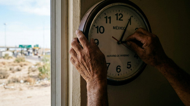 Manos ajustando un reloj análogo de pared atrasando una hora por el horario de invierno en la frontera norte
