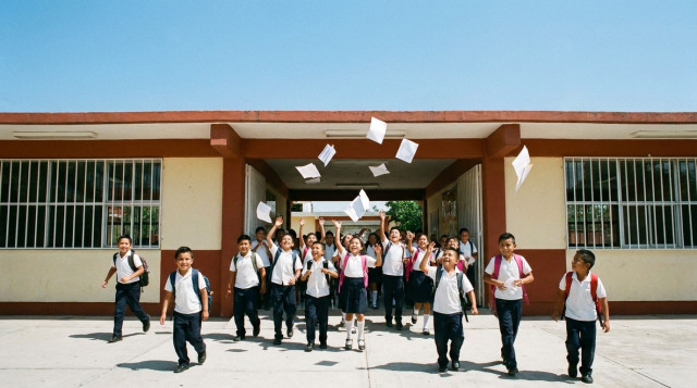 Estudiantes de primaria en México saliendo de la escuela con mochilas y sonriendo, celebrando el inicio de las vacaciones de verano bajo un cielo despejado