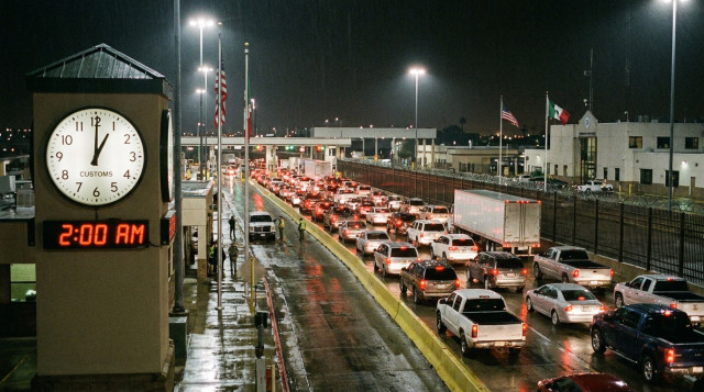 Reloj analógico marcando las dos de la madrugada en una garita de cruce fronterizo entre México y Estados Unidos con vehículos en espera