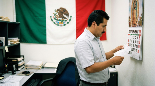 Trabajador revisando nómina y calendario laboral en oficina mexicana con bandera nacional de fondo