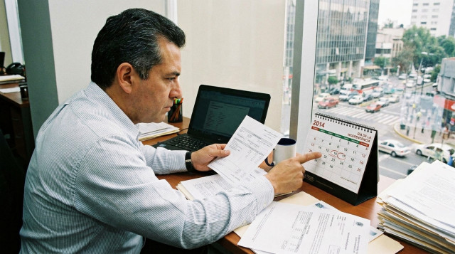 Trabajador de oficina revisando su recibo de nómina y calendario sobre un escritorio profesional