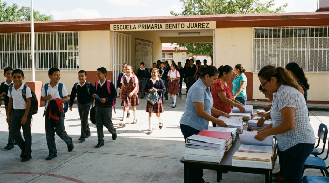 Alumnos de educación básica saliendo de la escuela y docentes organizando carpetas para el Consejo Técnico Escolar