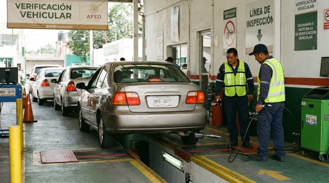 vehículo particular en la línea de inspección de emisiones de un verificentro con técnicos revisando el escape